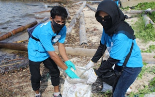 Hospitality workers lift a sack of collected marine debris from a beach in eastern Bintan, Indonesia.