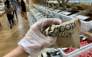 A customer using a disposable plastic glove holds a paper bag of products at a Scoop store in Singapore.
