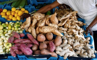 Vegetables and fruits, including manioc and sweet potatoes, are displayed in a grocery store