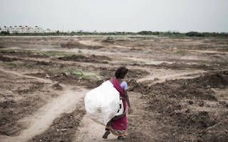 A woman walks into dried-up Narayanapuram Lake to collect waste to be sold in the scrap market