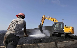 worker sprays water over piles of coal as a bulldozer shifts coal at Mundra Port Coal Terminal