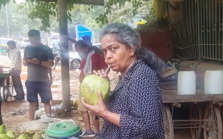 A woman sips from a fresh coconut using a plastic straw outside New Delhi's Jahanpannah forest park.
