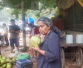 A woman sips from a fresh coconut using a plastic straw outside New Delhi's Jahanpannah forest park.