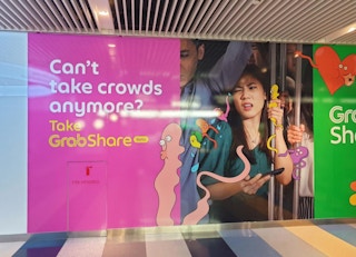 An outdoor advertisement for ride-hailing service Grab highlights the congestion and discomfort of taking public transport in Singapore.