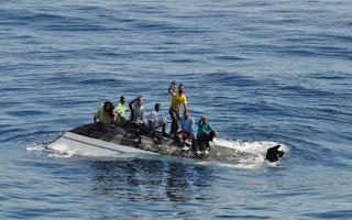 migrants on top of a capsized vessel