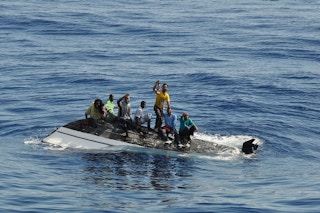 migrants on top of a capsized vessel