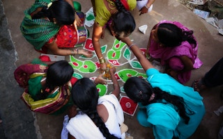 Women drawing rangoli on the floor in India