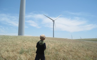 A child looks up at wind turbines