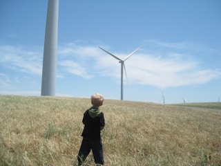 A child looks up at wind turbines
