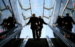 Business man and business woman on an escalator against blue sky