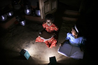Girls in a village in India read books after dark with the help of solar lamps