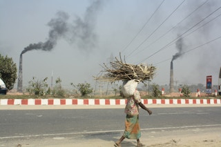 A man carries firewood past the smoking stacks of brick kilns Dhaka