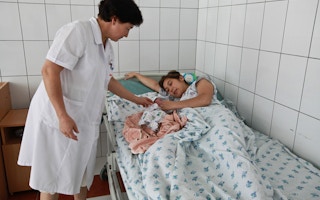 A women lies next to her newborn child in a hospital.